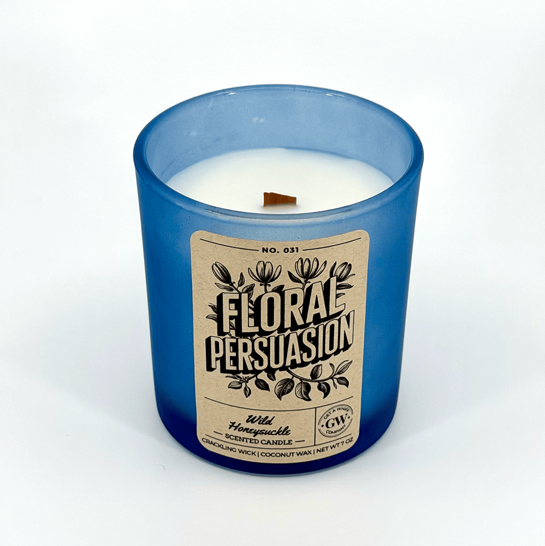 Candle with a blue glass container and 'Floral Persuasion' label on a white background