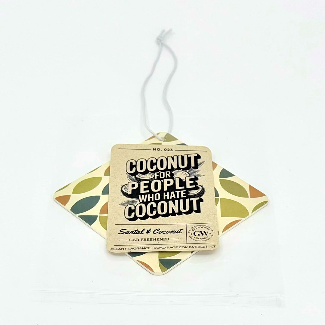 A car freshener tag labeled 'COCONUT FOR PEOPLE WHO HATE COCONUT' by GW, placed on top of a diamond-shaped patterned insert with olive and beige leaf motifs on a white background.