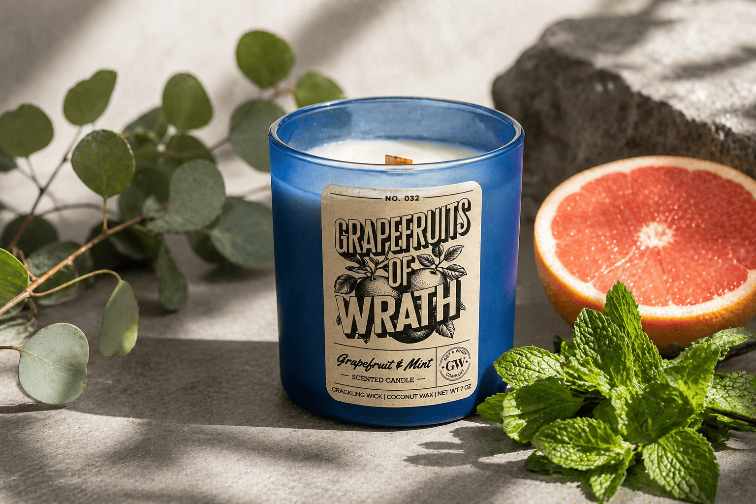 Grapefruit-scented candle with a label in a blue container, surrounded by green leaves and a half-cut grapefruit.