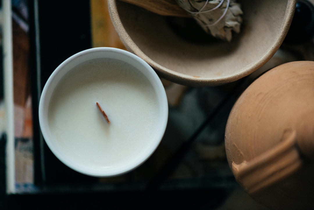 White candle in a small white bowl with a wooden lid on a dark surface.